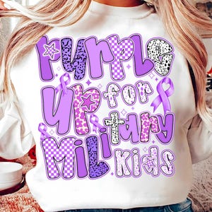 May include: White sweatshirt with a purple design that says "Purple Up for Military Kids". The design features a variety of patterns, including polka dots, checkered, and animal print.
