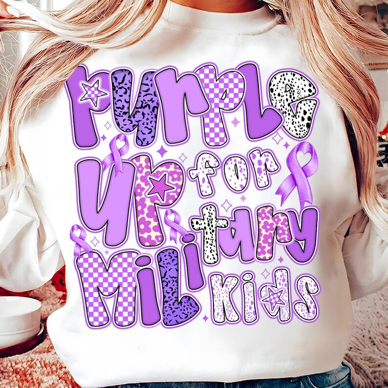 May include: White sweatshirt with a purple design that says "Purple Up for Military Kids". The design features a variety of patterns, including polka dots, checkered, and animal print.