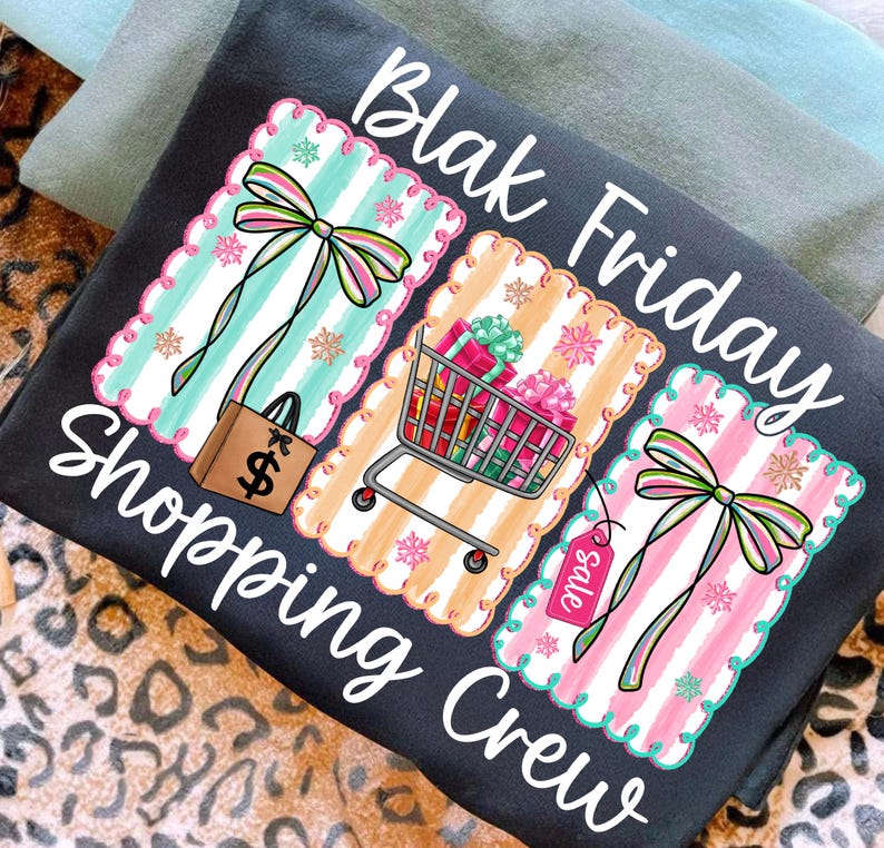 May include: Dark gray t-shirt with the words "Blak Friday Shopping Crew" in white script. The shirt features three decorative panels with shopping-themed graphics, including a shopping bag, shopping cart, and sale tag.