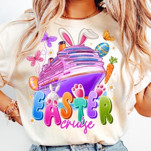 Pode incluir: Uma camiseta branca com um design gráfico colorido que apresenta um navio de cruzeiro com orelhas de coelho, ovos de Páscoa, cenouras e o texto "Easter Cruise".