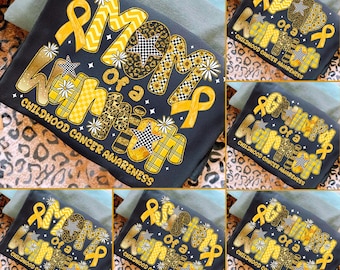 May include: Dark gray t-shirt with the text "Mom of a Warrior" in yellow, black, and white patterns, including stars, ribbons, and the words "Childhood Cancer Awareness."