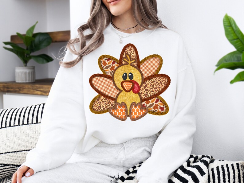 May include: White sweatshirt featuring a charming patchwork turkey design. The turkey is brown, yellow and orange with a red wattle. The design is ideal for Thanksgiving.