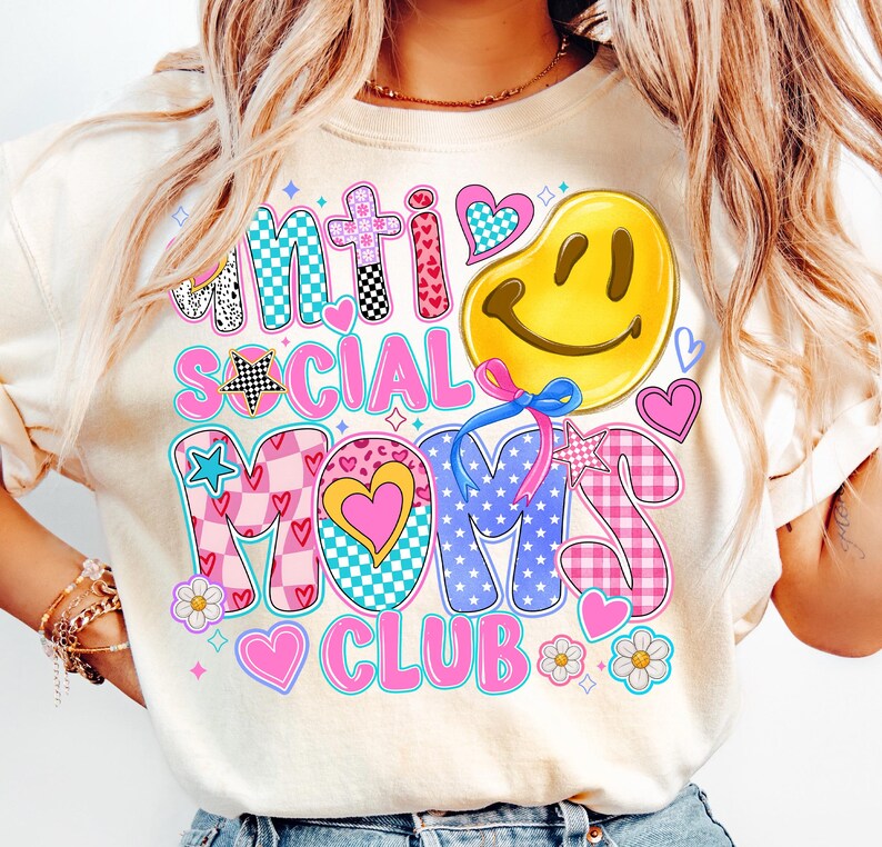 May include: A white t-shirt with a colorful graphic design that says "Anti Social Mom's Club". The design features a smiley face, stars, hearts, and checkered patterns.