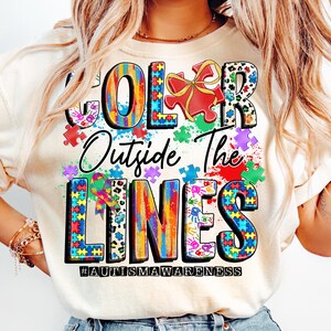 May include: A white t-shirt with a colorful graphic design that says "Color Outside The Lines" with puzzle pieces and the hashtag #autismawareness.