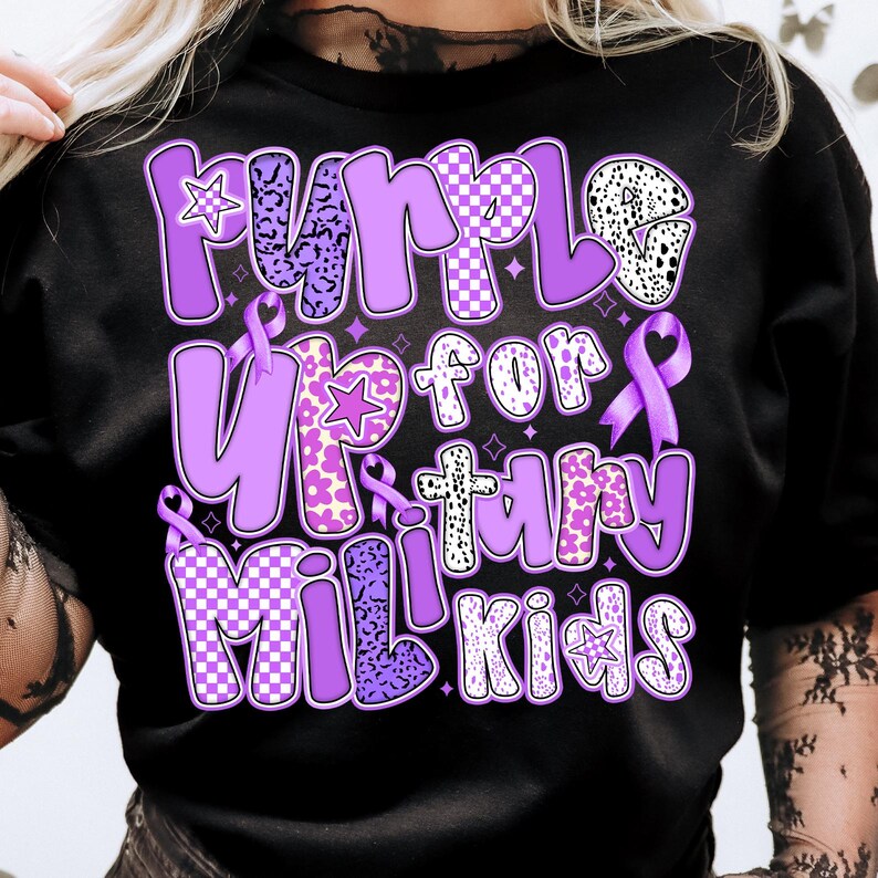 May include: Purple Up for Military Kids t-shirt with a purple, white and black chequered pattern, leopard print and flowers. The shirt has a purple ribbon and stars.
