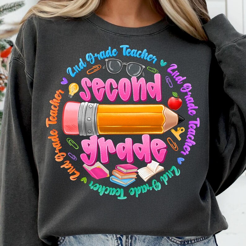 May include: Dark gray sweatshirt with a colorful graphic for a 2nd grade teacher. The design includes a large pencil, the words "second grade", and other school-related icons. The text "2nd Grade Teacher" is in a circle around the design.