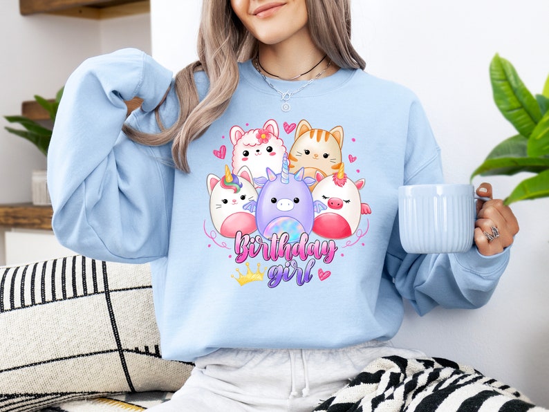 Puede incluir: Sudadera azul claro con un gr&aacute;fico de un unicornio, un gato y otros animales lindos. El texto "birthday girl" est&aacute; impreso debajo de los animales.
