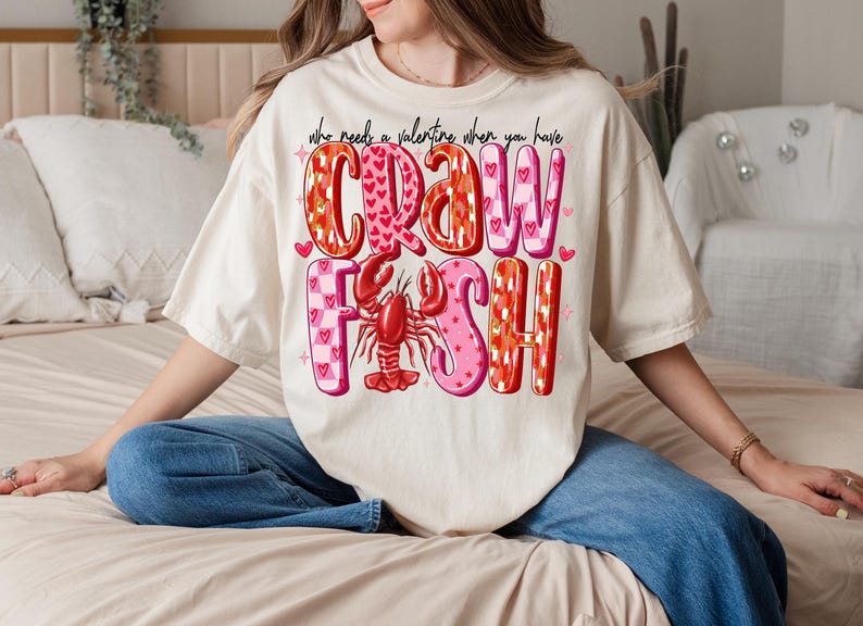 May include: A white t-shirt with a pink and red graphic that says "Who needs a valentine when you have crawfish".