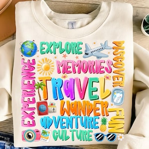 May include: A white sweatshirt with a colorful graphic design featuring the words "Explore", "Memories", "Travel", "Wander", "Adventure", "Culture", "Discover", "Fun", and "Experience". The graphic also includes a globe, airplane, sun, palm trees, pineapple, sunglasses, and a camera.