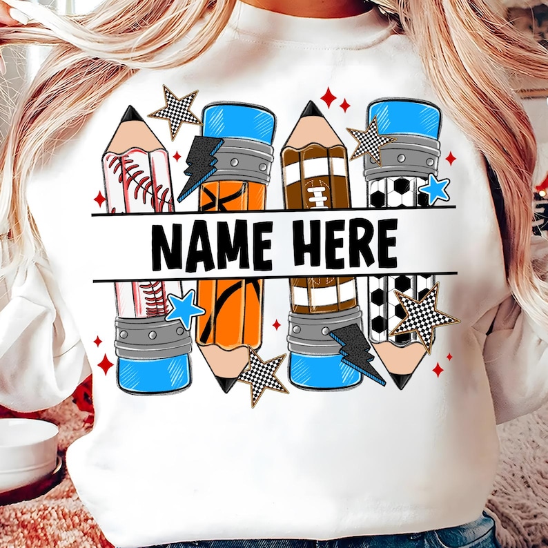 Pode incluir: Camisola branca com um design de l&aacute;pis com temas desportivos. O design inclui elementos de basebol, basquetebol e futebol, juntamente com o texto "NAME HERE" em preto. Acentuado com estrelas e raios.