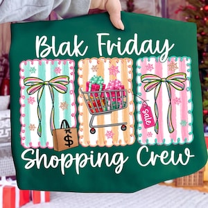 May include: Green fabric with the words "Blak Friday Shopping Crew" in white script. The design includes three rectangular panels with striped backgrounds, bows, a shopping cart filled with gifts, and a shopping bag.