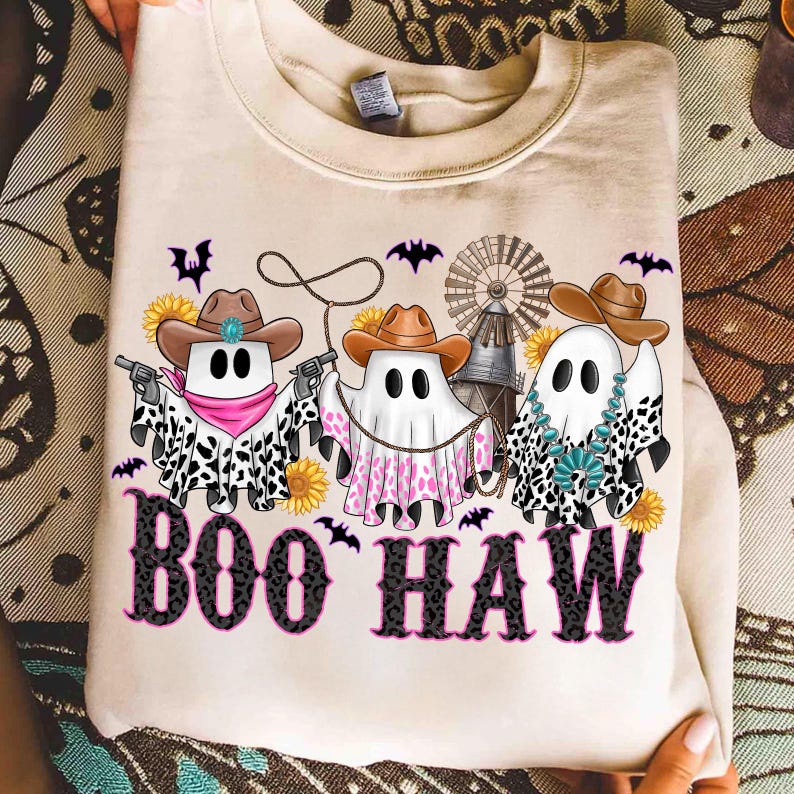 May include: A beige sweatshirt featuring a "Boo Haw" design. The design includes three ghost figures wearing cowboy hats and bandanas, holding guns and lassos. The ghosts are surrounded by bats, sunflowers, and a windmill.