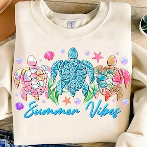 May include: A cream colored sweatshirt with a graphic of three colorful sea turtles and the text "Summer Vibes".