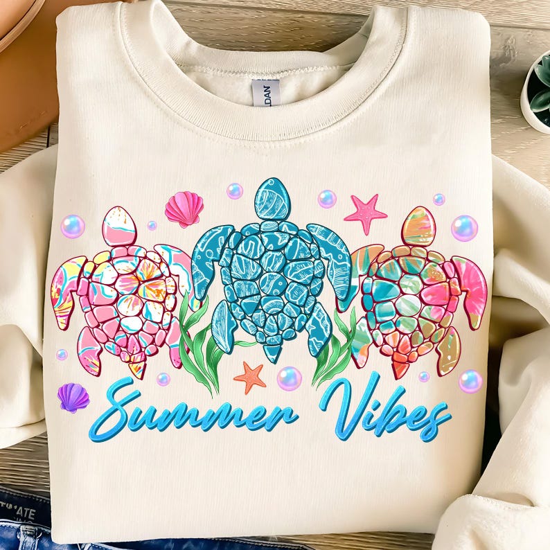May include: A cream colored sweatshirt with a graphic of three colorful sea turtles and the text "Summer Vibes".