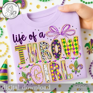 May include: A lilac t-shirt featuring the phrase "life of a THROW GIRL" in a vibrant, decorative style. The design incorporates Mardi Gras colours and patterns, including purple, green, and gold. The shirt is decorated with a bow and fleur-de-lis.
