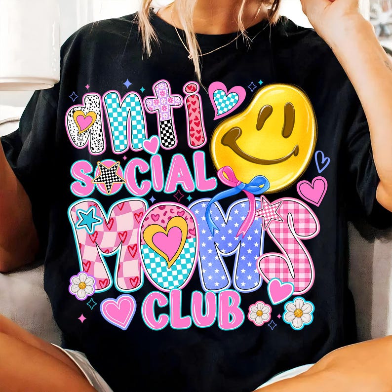 May include: Black t-shirt with a colorful graphic design that says "Anti Social Moms Club". The graphic features a smiley face, stars, hearts, and checkered patterns.