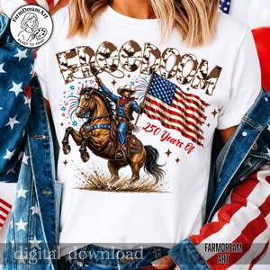 May include: White t-shirt featuring a cowboy riding a horse, holding an American flag. The word "FREEDOM" is above the image, with "250 Years Of" below. The design includes fireworks and stars, celebrating American heritage.