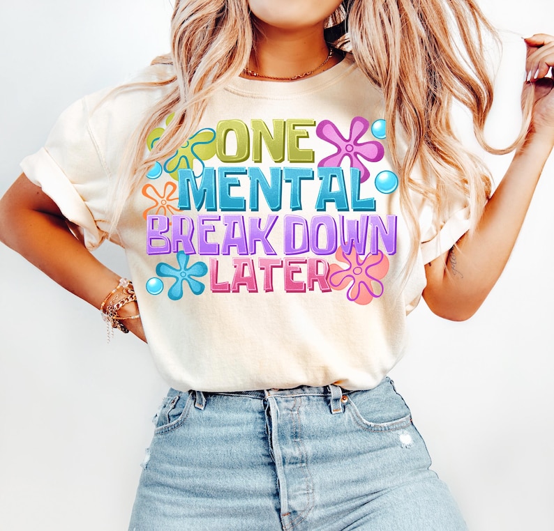 May include: A white t-shirt with a graphic design featuring colorful flowers and the text "One Mental Break Down Later".