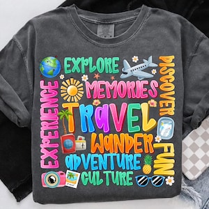 May include: A dark gray t-shirt with a colorful graphic design featuring the words "Explore", "Memories", "Travel", "Wander", "Adventure", "Culture", "Discover", "Fun", and "Experience". The graphic also includes images of a globe, a plane, a sun, a palm tree, a pineapple, sunglasses, and a camera.