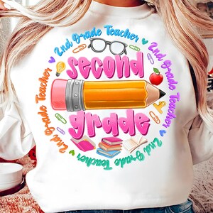 May include: White sweatshirt with a colorful graphic design for a 2nd Grade Teacher. The design includes a large pencil, the words "Second Grade", and other school-related icons like glasses, books, and an apple.