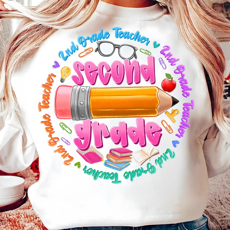 May include: White sweatshirt with a colorful graphic design for a 2nd Grade Teacher. The design includes a large pencil, the words "Second Grade", and other school-related icons like glasses, books, and an apple.