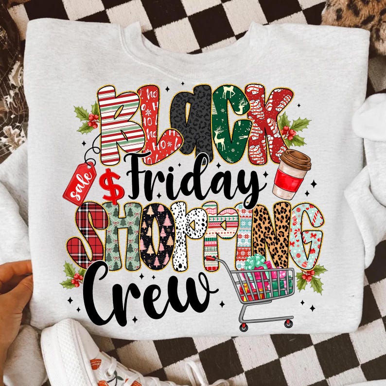 May include: A light gray sweatshirt with a colorful graphic that reads "Black Friday Shopping Crew." The text incorporates various patterns, including stripes, leopard print, and holiday designs. A shopping cart filled with gifts is also featured.