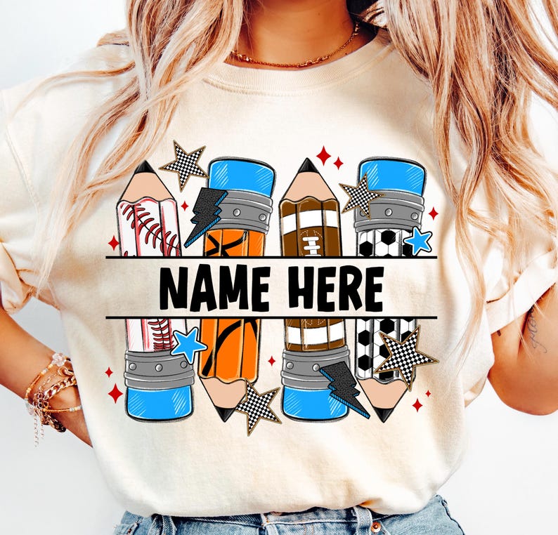 Pode incluir: Camiseta creme com um design de l&aacute;pis que incorpora elementos esportivos. O design inclui gr&aacute;ficos de beisebol, basquete e futebol, juntamente com o texto "NAME HERE". Os detalhes incluem estrelas e raios.