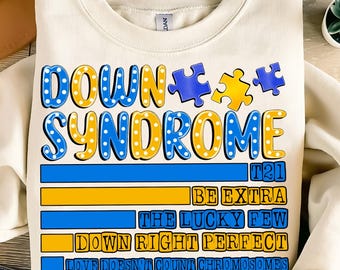 Pode incluir: Uma camisola de cor creme com o texto "DOWN SYNDROME" em letras azuis e amarelas com peças de puzzle. O texto "T21" está em azul e amarelo. O texto "BE EXTRA THE LUCKY FEW DOWN RIGHT PERFECT LOVE DOESN'T COUNT CHROMOSOMES" está em azul e amarelo.