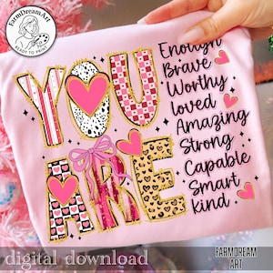 May include: A pink t-shirt with the words "YOU ARE" in a decorative font, featuring hearts and a bow. The words "Enough, Brave, Worthy, Loved, Amazing, Strong, Capable, Smart, Kind" are also printed on the shirt. The words "digital download" are at the bottom.