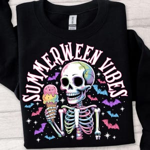 May include: Black sweatshirt with a colorful skeleton graphic holding an ice cream cone. The design includes the text "SUMMERWEEN VIBES" in a curved font, with bats and stars. The skeleton's skull has a rainbow gradient.