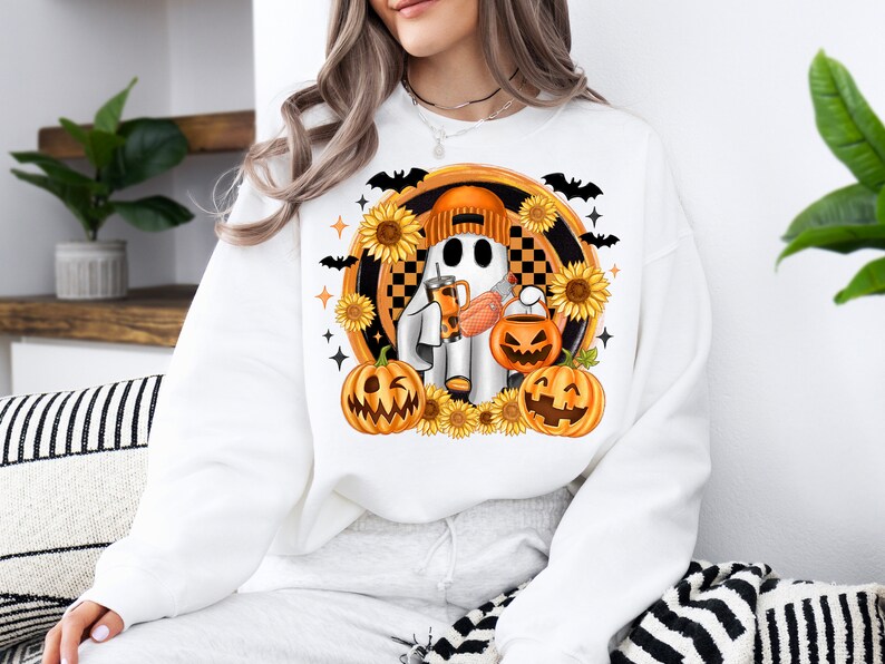 Peut inclure: Sweat-shirt blanc avec un motif sur le th&egrave;me d'Halloween. Le motif comprend un fant&ocirc;me portant un bonnet orange, tenant une boisson et une lanterne citrouille. Des tournesols, des chauves-souris et des &eacute;toiles entourent le fant&ocirc;me et les citrouilles.