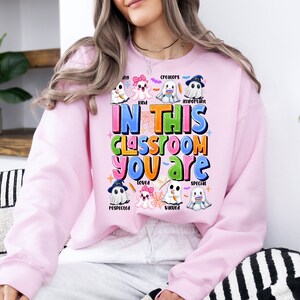 May include: Pink sweatshirt with a ghost theme. The text reads "In this classroom you are" with words like "kind", "creators", "important", "loved", "respected", "valued", and "special" around the ghosts.