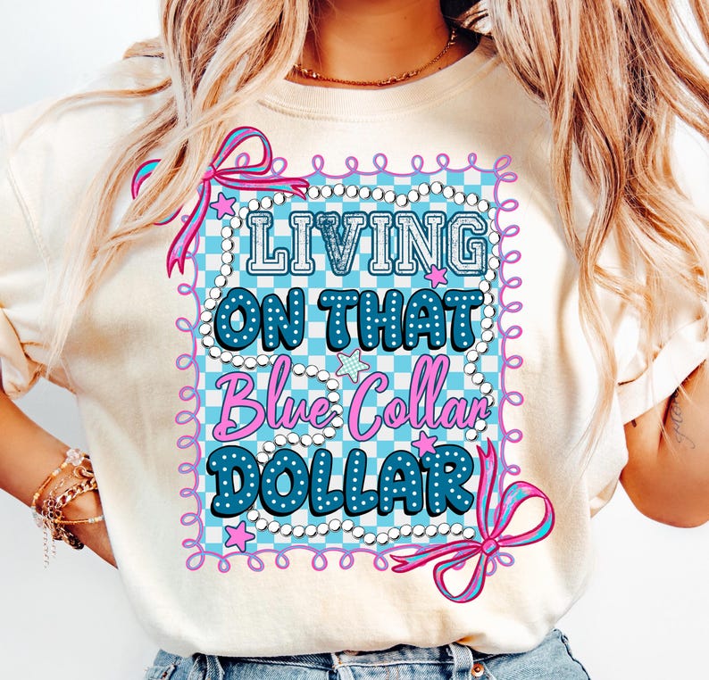 Pu&ograve; includere: T-shirt color crema con una grafica che recita "LIVING ON THAT Blue Collar DOLLAR" in blu e rosa. Il design presenta uno sfondo a scacchi, stelle e bordi decorativi.