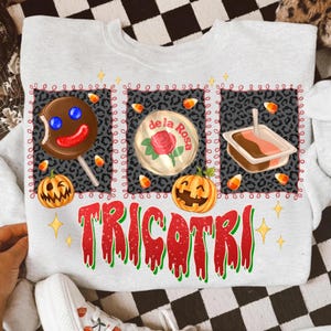 K&ouml;nnte beinhalten: Ein hellgraues Sweatshirt mit einem Halloween-Motiv. Das Design umfasst einen Lolli, eine S&uuml;&szlig;igkeit und ein Dessert, jeweils umrahmt von einem Leopardenmuster. Das Wort "TRICOTRI" ist in Rot und Gr&uuml;n gedruckt.