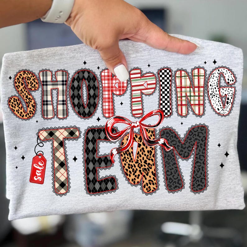 Peut inclure: Un t-shirt gris clair avec l'inscription "SHOPPING TEAM" dans diff&eacute;rents motifs, notamment &agrave; carreaux, l&eacute;opard et pois. Un n&oelig;ud rouge et une &eacute;tiquette "soldes" sont &eacute;galement pr&eacute;sents dans le design.
