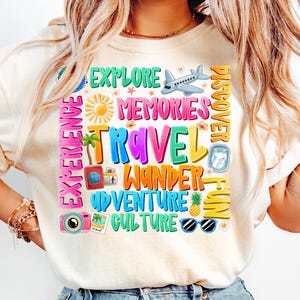 May include: A white t-shirt with a colorful graphic design featuring the words "Explore", "Memories", "Travel", "Wander", "Adventure", "Culture", "Discover", "Fun", and "Experience". The graphic also includes a plane, a compass, a camera, sunglasses, a pineapple, and palm trees.
