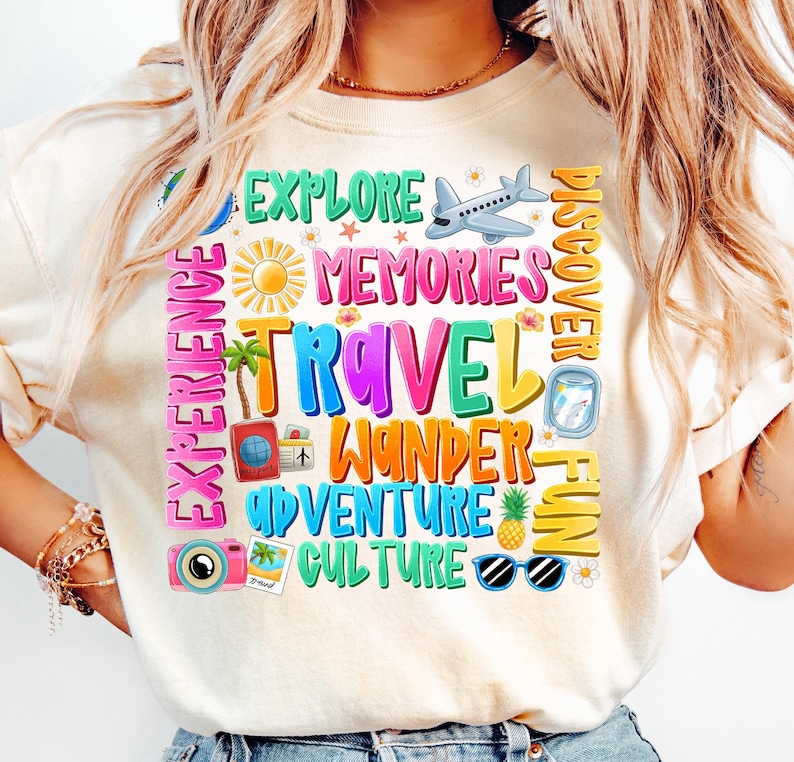 May include: A white t-shirt with a colorful graphic design featuring the words "Explore", "Memories", "Travel", "Wander", "Adventure", "Culture", "Discover", "Fun", and "Experience". The graphic also includes a plane, a compass, a camera, sunglasses, a pineapple, and palm trees.