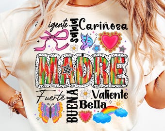 May include: A white t-shirt with a colorful graphic design that says "MADRE" in large letters. The design also includes butterflies, hearts, stars, and the words "Cariñosa", "Valiente", "Bella", "Buena", and "Fuerte".