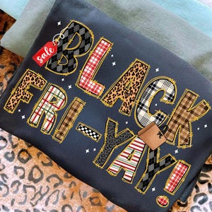 May include: A dark gray sweatshirt with the words "BLACK FRIDAY YAY!" in a mix of patterns, including leopard print, plaid, and stripes. A red "sale" tag hangs from the letter "B".