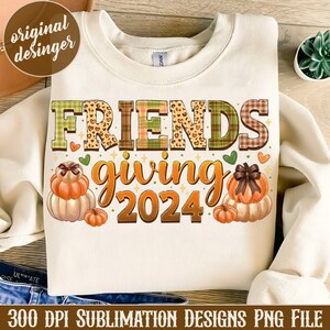 May include: A white sweatshirt featuring the text "FRIENDSgiving 2024" in colourful patchwork letters. The letters are decorated with hearts, stars, and a leopard print. The design also includes three pumpkins with bows.