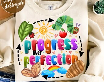 Puede incluir: Una sudadera de color crema con un diseño gráfico colorido que presenta el texto "Progress over Perfection". El diseño incluye una oruga, un arcoíris, mariposas y otros elementos caprichosos.
