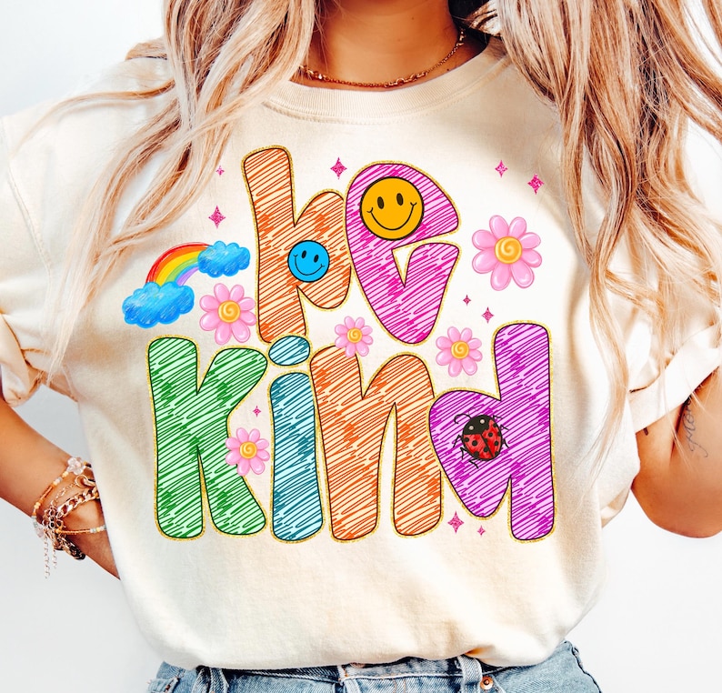 May include: Cream-colored sweatshirt with the words "be kind" in colorful, outlined letters. The design includes a rainbow, flowers, smiley faces, and a ladybug. The graphic is in a retro, groovy style.