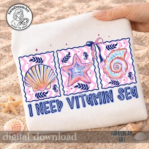Pu&ograve; includere: Un telo da mare bianco con un design colorato raffigurante una conchiglia, una stella marina e una conchiglia a spirale, con la scritta "I NEED VITAMIN SEA". Il design include accenti rosa e blu, cavallucci marini e un fiocco.
