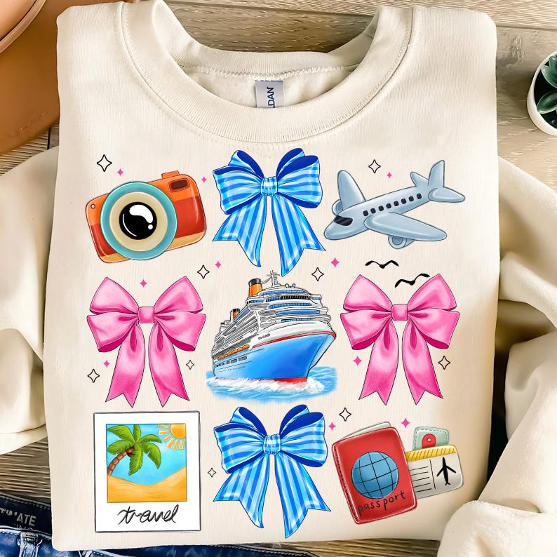 Puede incluir: Una sudadera beige con tem&aacute;tica de viaje. Presenta un crucero, un avi&oacute;n, una c&aacute;mara, un pasaporte, una palmera y lazos azules y rosas.