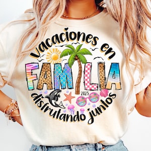 Op de afbeelding: Een wit T-shirt met een kleurrijk grafisch ontwerp met de tekst "Vacaciones en Familia disfrutando juntos" met een palmboom, een zon, een walvis, een ster en schelpen. Het jaar 2025 is ook opgenomen in het ontwerp.