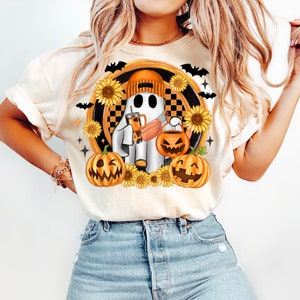 Peut inclure: T-shirt cr&egrave;me avec un motif d'Halloween. Le motif comprend un fant&ocirc;me portant un bonnet orange, tenant une boisson et un seau &agrave; bonbons en forme de citrouille, entour&eacute; de tournesols, de citrouilles et de chauves-souris. Le fant&ocirc;me est plac&eacute; sur un fond &agrave; carreaux.