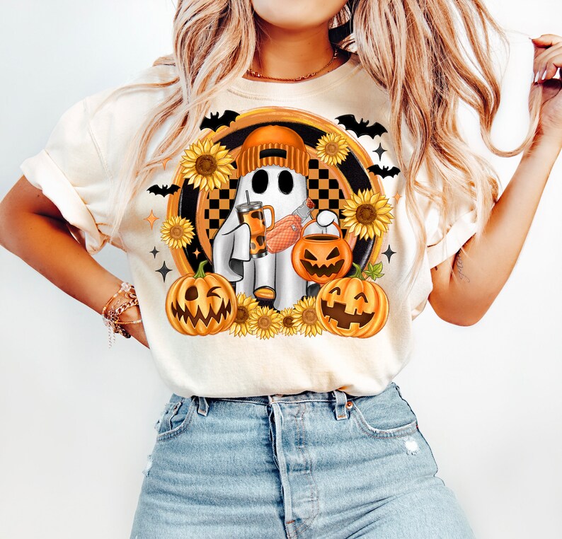 Peut inclure: T-shirt cr&egrave;me avec un motif d'Halloween. Le motif comprend un fant&ocirc;me portant un bonnet orange, tenant une boisson et un seau &agrave; bonbons en forme de citrouille, entour&eacute; de tournesols, de citrouilles et de chauves-souris. Le fant&ocirc;me est plac&eacute; sur un fond &agrave; carreaux.