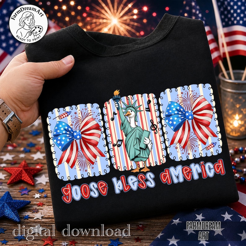 May include: Black t-shirt with a patriotic design featuring a goose dressed as the Statue of Liberty, surrounded by red, white, and blue bows and fireworks. The text "goose bless america" is displayed in a playful font.