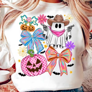 May include: White sweatshirt with a Halloween design. The graphic shows a ghost in a cowboy hat with guns, alongside pumpkins, bows, flowers, bats, and stars. The pumpkin is pink and checkered.