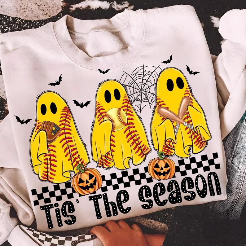 Puede incluir: Sudadera crema con un dise&ntilde;o de Halloween. Presenta tres figuras de fantasmas amarillos con costuras de b&eacute;isbol, sosteniendo equipo de b&eacute;isbol. El dise&ntilde;o incluye calabazas, murci&eacute;lagos y el texto "Tis The season" en negro.